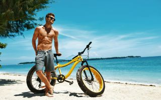 накаченный мужчина на пляже с велосипедом фет байком